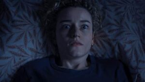 a short-haired blonde woman who is visibly distressed or shocked laying on a patterned cushion.